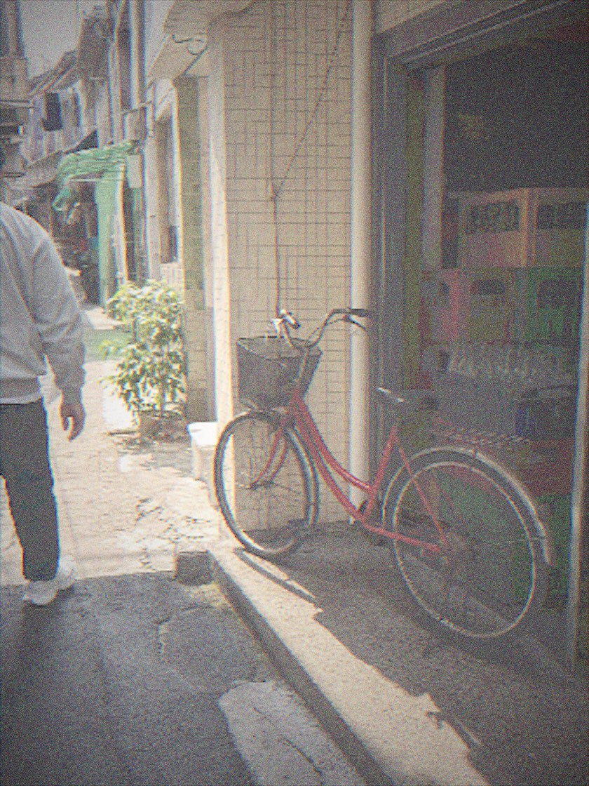 CCD Camera 用 POCKET 档案拍出的街巷照片，红色自行车靠在店铺门口，画面带有低像素颗粒和轻微偏色。